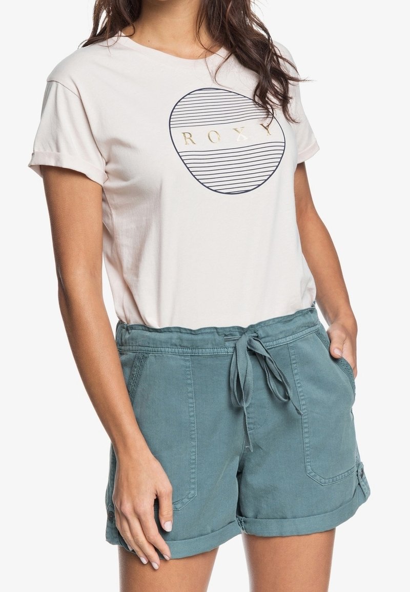 Světle růžové tričko s kruhovým námořnicky modrým vzorem a zlatým textem, doplněné o tyrkysové šortky s páskem na zavazování, ohrnovacími lemy a kapsami.