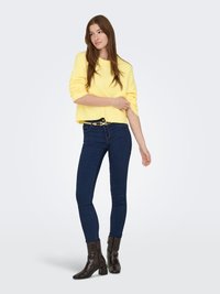 Suéter amarillo corto con cuello redondo, combinado con jeans pitillo azul oscuro y botines negros con textura de cocodrilo.
