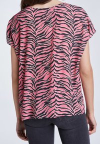 Haut rose à manches courtes avec un motif à rayures zébrées noir et blanc. Texture douce, coupe ample et ourlet arrondi, convient pour un style décontracté.