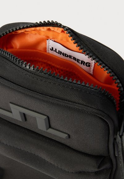 Μαύρο υφασμάτινο πορτοφολάκι με φερμουάρ, με λαμπερό πορτοκαλί εσωτερικό και εμφανές ετικέτα J.LINDEBERG μέσα στο κεντρικό διαμέρισμα.