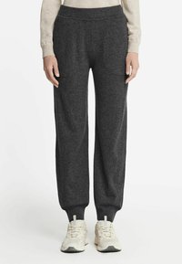 Mørkegrå sweatpants lavet af blødt stof, med elastisk talje, sidelommer og smalle manchetter. Båret med lyse sneakers.