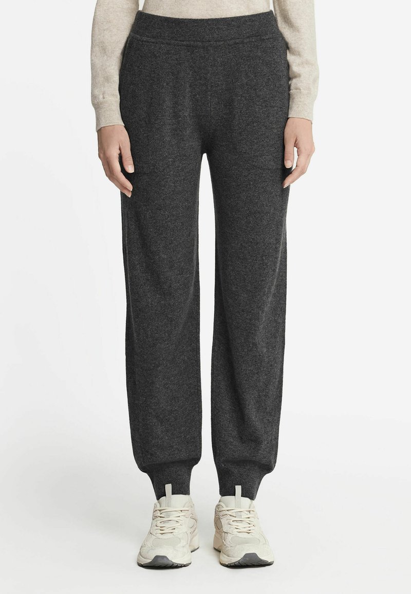 Mørkegrå sweatpants lavet af blødt stof, med elastisk talje, sidelommer og smalle manchetter. Båret med lyse sneakers.