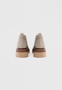 Bottes chevilles en daim beige avec un bout arrondi, un talon texturé, des accents en bois et des semelles en caoutchouc contrastées. Vue arrière dévoilant des coutures à motifs.