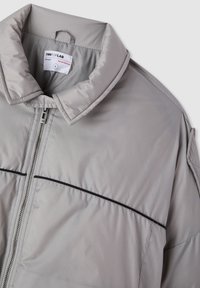 Giubbotto imbottito grigio chiaro con zip frontale, colletto alto, piping nero sul petto e etichetta del designer all'interno del colletto.