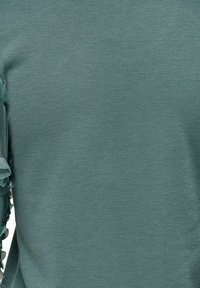 Maglione in cotone color teal con finitura testurizzata e dettagli arricciati lungo la manica sinistra. Tessuto morbido e leggero con scollatura a girocollo.