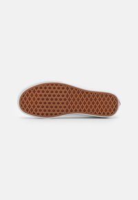 White sneaker sole with a brown rubber traction pattern featuring a honeycomb design, outlining the shoe's shape and cushioning features.