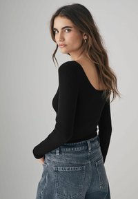 Sort langærmet top med en scoop ryg, lavet af ribbet stof. Sammen med højderede, falmede blå denim jeans.
