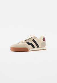 Beige Wildleder-Sneaker mit schwarzen Streifen, leichter Gummisohle und weinrotem Akzent an der Ferse. Mit flachen Schnürsenkeln und kontrastierenden Nähten.