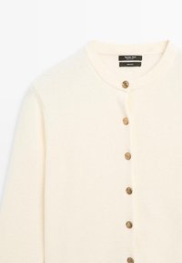 Cardigan en laine crème avec un col rond, des poignets côtelés et cinq boutons dorés à l'avant. Texture lisse avec un minimum de détails.