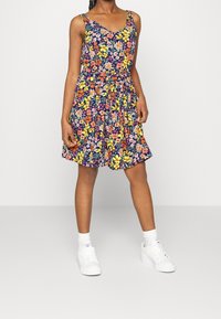 Květinové šaty s námořnickým pozadím, zdobené živými žlutými, růžovými a bílými květinami. Bezramenný design, zúžený pas, hravá sukně.