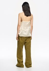 Camiseta de satén crema con tirantes finos; pantalones texturizados de corte relajado en verde oliva. Se ve la espalda del modelo, destacando los detalles de la parte superior y los pantalones.