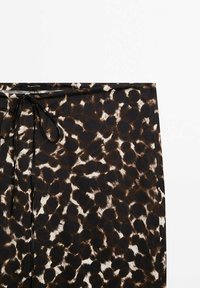 Gros plan sur une jupe imprimé léopard marron et noir avec un fin cordon noir à la taille, présentée sur fond blanc.
