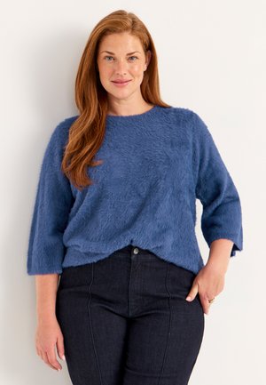 Blauwe, donzige gebreide trui met driekwartmouwen en een ronde halslijn, gecombineerd met donkere spijkerbroek. Eenvoudig, casual ontwerp.