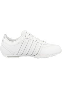 Weißer Sportschuh mit einem glatten Lederoberteil, sechs Schnürösen und drei horizontalen Streifen an der Seite. Gepolsterter Kragen und Gummisohle.