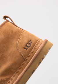 Stivaletto alla caviglia in suede beige con cuciture, logo laterale, parte superiore testurizzata e suola in gomma con intagli per la presa.