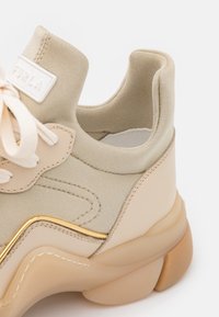 Beige högklackade sneakers med ovandel i mjukt tyg, guldaccenter och en klumpig, genomskinlig sula. Har snörningsdesign och vadderad krage.
