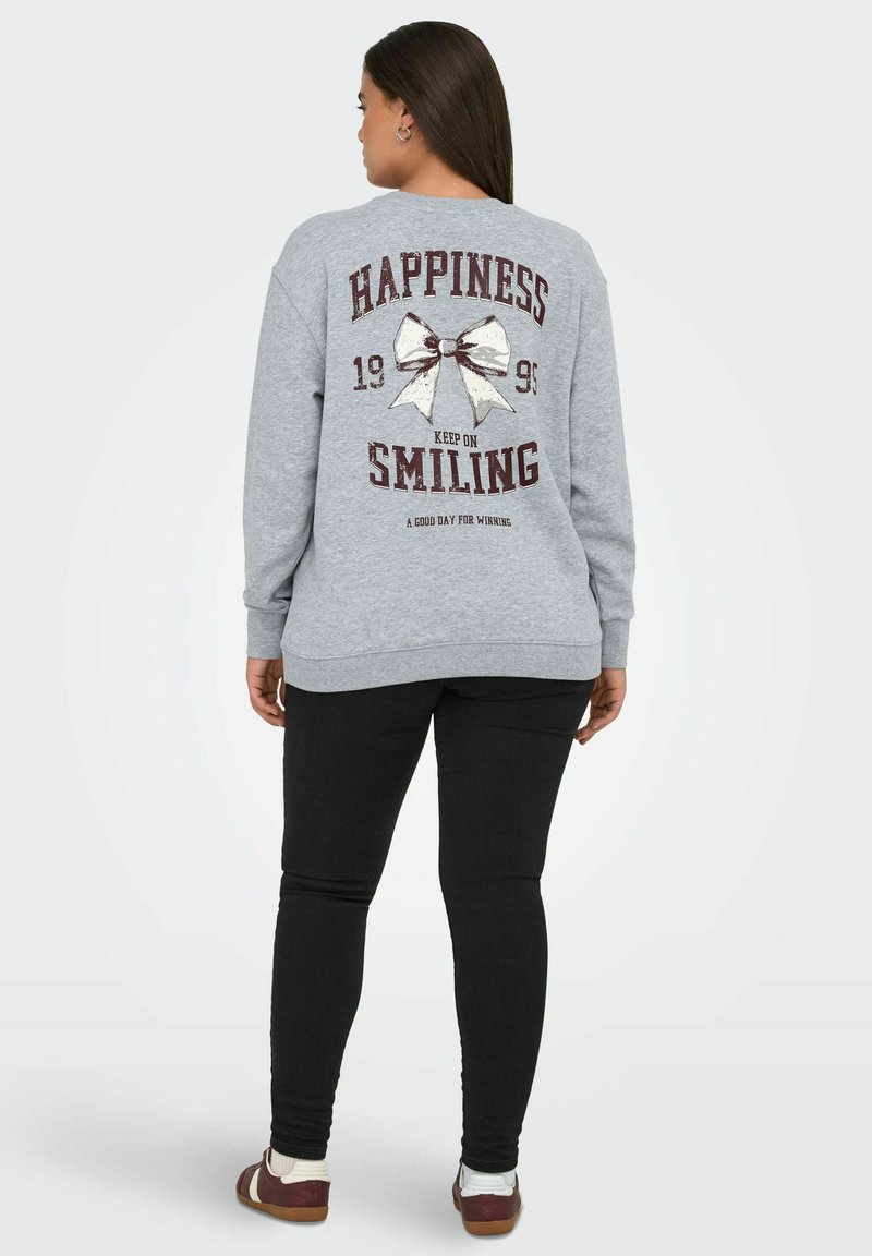 Felpa grigia con un design stampato che presenta le parole "FELICITÀ," un'illustrazione di un fiocco e "CONTINUA A SORRIDERE." Abbinata a leggings neri.