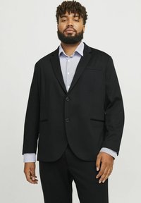 Svart blazer med två knappar, slagkrage och två framfickor. Bärs över en ljusblå randig skjorta med kontrasterande manschetter.