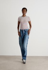 Striped short-sleeve shirt with red, blue, and green stripes, paired with loose-fit faded blue jeans and black-and-white sneakers.