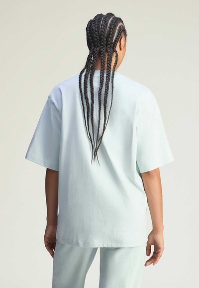 Hellmintgrünes, übergroßes T-Shirt aus Baumwolle, kurze Ärmel, rundem Ausschnitt, mit glatter Textur und minimalistischem Design. Rückansicht zeigt geflochtenes Haar.