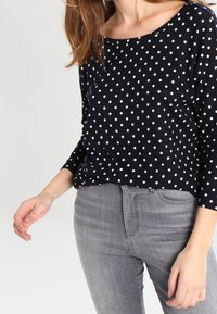 Tummansininen pilkkupaita, joka on valmistettu kevyestä kankaasta, jossa on leveä pääntie ja kolmannes-osa hihat, yhdistettynä harmaisiin slim fit -farkkuihin.