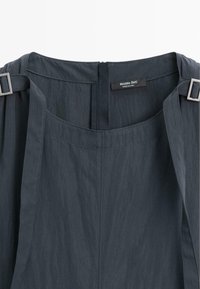 Tmavě šedé šaty bez rukávů se čtvercovým výstřihem, nastavitelné ramenní popruhy se stříbrnými přezkami a viditelná značka Massimo Dutti uvnitř.