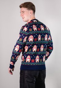 Marineblauer Pullover mit einem festlichen Bärenmuster, roten und grünen Geschenkbrettern sowie Schneeflocken. Rippstrickbündchen und -saum sorgen für ein vollendetes Erscheinungsbild.