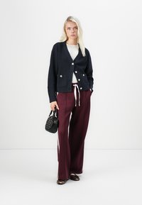Navy knitted cardigan with buttons and front pockets, paired with maroon wide-leg trousers featuring white stripes and a black handbag.