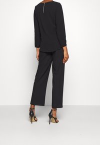 Top nero a maniche lunghe con zipper sulla schiena, abbinato a pantaloni neri a gamba larga e sandali con tacco a strappo. Tessuto liscio, silhouette moderna.