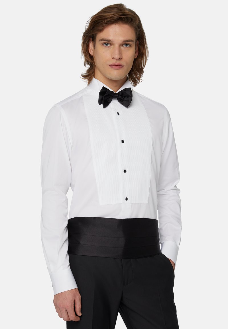 Chemise de smoking blanche avec un devant plissé, nœud papillon noir et ceinture en satin noire. Dotée de boutons noirs et de poignets nets.