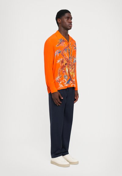 Oranges Langarmshirt mit einem Tiger-Graphic und Blumenmustern, kombiniert mit navyfarbenen Hosen und weißen Sneakers. Glatte Textur, lässige Passform.