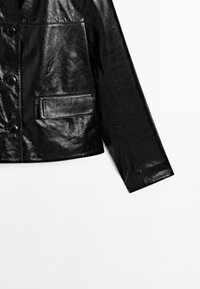 Giacca di pelle nera con una texture lucida, caratterizzata da grandi bottoni neri e una singola tasca frontale. Vestibilità su misura con taglio dritto.