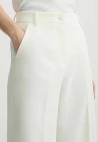 Witte wijde broek, op maat gemaakt, met zijzakken, een gladde textuur en een voorkleur met een rechthoekige knoop.