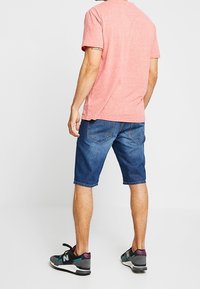 Pink heathered t-shirt, blue denim shorts, and black athletic shoes with purple and teal accents. Short sleeves and relaxed fit.
