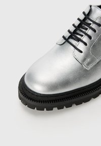 Zilveren leren veterschoenen met een ronde neus, textured zwarte rubberen zool en zwarte veters. Gladde metallic afwerking met gestikte accenten.