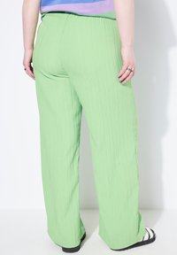 Lichtgroene, gestructureerde wijde broek met hoge taille. Zichtbare naden en een ontspannen fit. Gecombineerd met zwarte sandalen en een multicolore top.