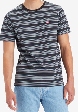 Mand iført en kortærmet T-shirt med sorte, blå, hvide og grå striber og et rødt Levi's-logo på brystet samt lyseblå jeans.