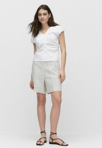 Witte blouse met korte mouwen en een V-hals, met geplooide zijkanten, gecombineerd met lichtbeige linnen shorts en zwarte gestrikte sandalen.