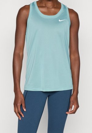 Persoon draagt een lichtblauw mouwloos Nike tanktop en donkerblauwe legging, staand tegen een effen witte achtergrond.