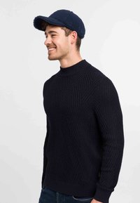 Maglione in maglia blu navy con un motivo geometrico e colletto alto. Abbinato a un cappello in pile blu navy con tesa piatta.