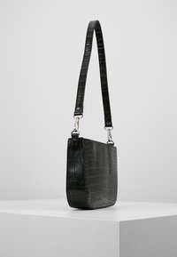 Svart krokodilpräglad läderväska med rektangulär form, justerbar rem och silverfärgad hårdvara, med en slät yta.