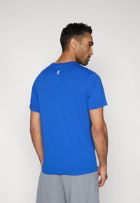 Blaues T-Shirt mit kurzen Ärmeln aus weichem Stoff, mit rundem Ausschnitt und kleinem Logoakzent am Hinterkragen.