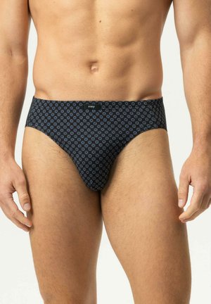 Männlicher Torso mit schwarzen Slips mit kleinem blauem geometrischem Muster und kleinem Logoschild in der Mitte des Bunds.