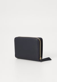 Portefeuille en cuir noir avec une texture lisse, de forme rectangulaire, avec des fermetures éclair en or et une petite étiquette en cuir attachée à la tirette.