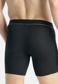 Boxer in cotone nero con design aderente. Tessuto liscio, vita elastica con un sottile dettaglio a righe. Lunghezza a metà coscia, senza motivi visibili.