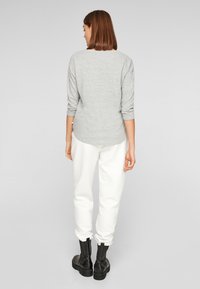 Grijze langek mouwtop met een ronde onderkant, gecombineerd met witte gestructureerde sweatpants en zwarte enkellaarzen. Achteraanzicht toont een ontspannen pasvorm en mouwen.