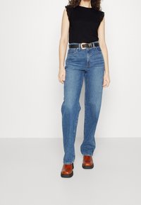 Sorte ærmeløs top med blonder, parret med højtaljede blå jeans og brune platform-sko, med et skinnende sort bælte.