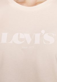 Vaaleanbeige puuvillainen T-paita, jossa on pyöreä kaula-aukko. Paidassa on suuri valkoinen Levi's-logo ja sen alla teksti "Since 1873".