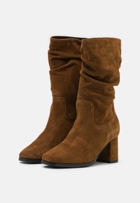 Brown suede mid-calf boots with slouchy shaft, block heels, rounded toes, and black rubber soles on a white background.