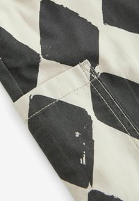 Black and cream fabric with a large geometric pattern featuring painted brush strokes. Includes a visible pocket and contrasting stitching.